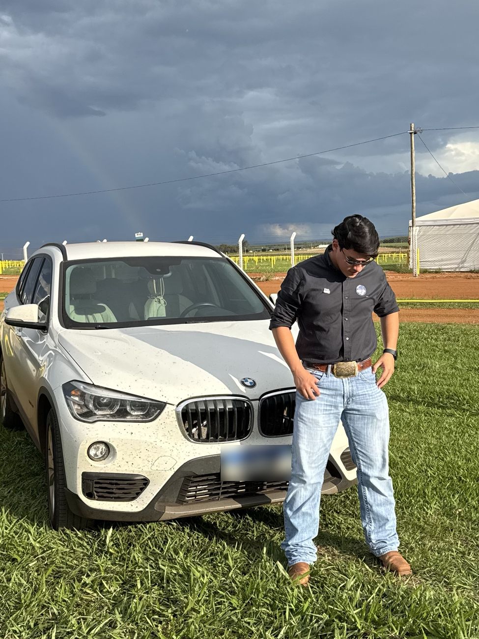 Wallas de camisa preta ao lado de um carro branco com céu de tempestade