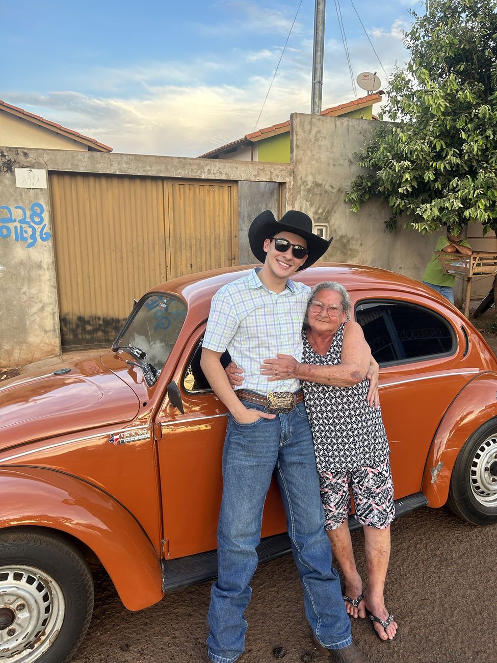 Wallas abraçado com uma senhora ao lado do fusquinha laranja