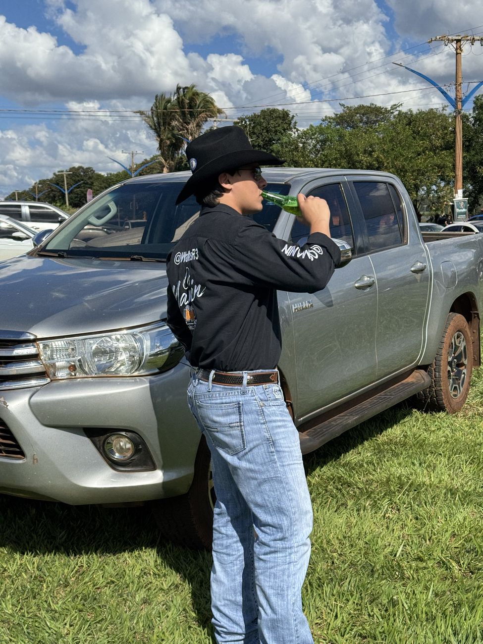 Wallas de chapéu preto bebendo ao lado de uma Hilux prata